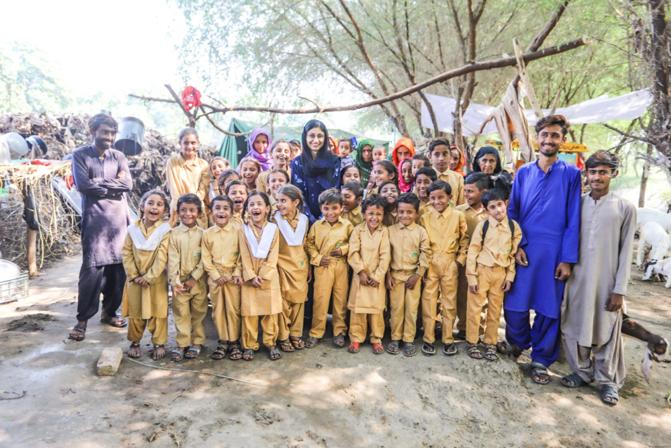 Group of children in uniform laughing and smiling alongside smiling adults.